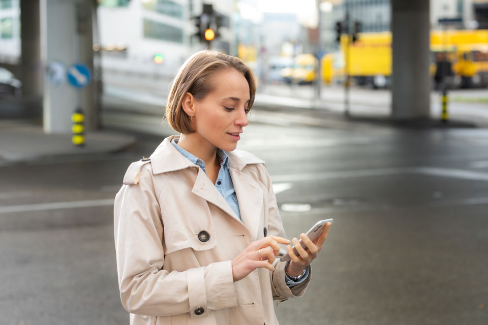 Eine Frau benutzt unterwegs ihr Smartphone, um eine Instant-Zahlung in Auftrag zu geben